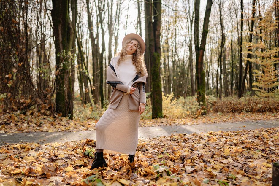 Young woman with curly hair smiling joyfully in an autumn park filled with colorful leaves